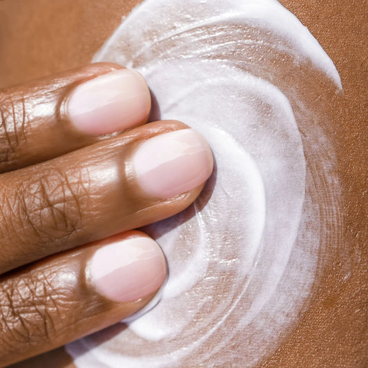 Hand applying white cream on a brown background