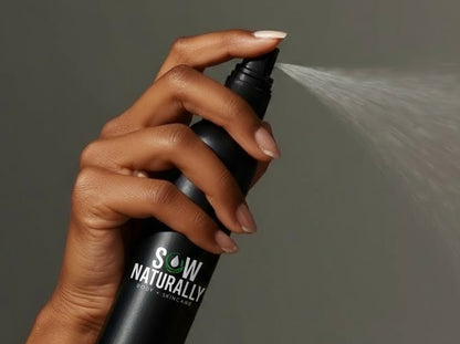 Hand holding a 'Sow Naturally' skincare product with a spray action against a neutral background
